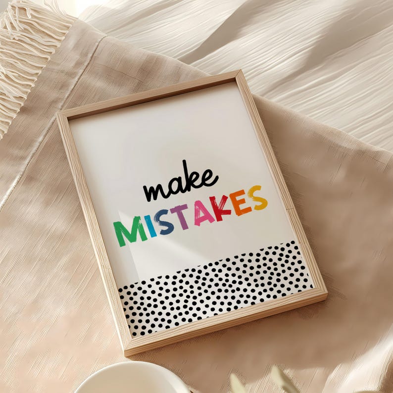 May include: A framed print with a white background and black polka dots at the bottom. The print says "make mistakes" in rainbow colors.