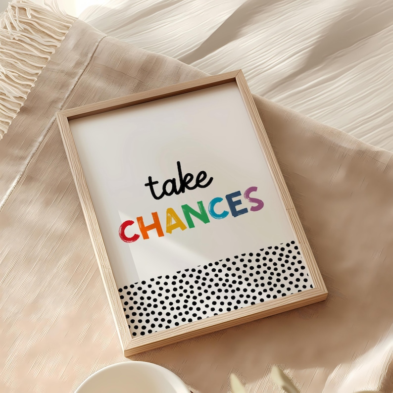 May include: A framed print with a white background and black polka dots at the bottom. The print features the text "take chances" in rainbow colors.