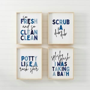 May include: Four framed prints with blue and white text on a white background. The prints feature bathroom-themed phrases: "So Fresh and So Clean", "Scrub a Dub Dub", "Potty Like a Rock Star", and "Splish Splash I Was Taking a Bath".