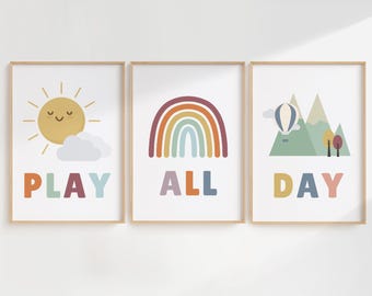 May include: Three framed prints with colorful illustrations and text. The first print features a yellow sun with a smiling face and a white cloud. The text reads "PLAY". The second print features a rainbow with red, orange, yellow, green, blue, indigo, and violet colors. The text reads "ALL". The third print features a green mountain range with a hot air balloon and trees. The text reads "DAY".