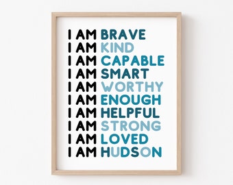 May include: A framed print with the words "I AM" followed by positive affirmations in black and blue text. The affirmations include "BRAVE," "KIND," "CAPABLE," "SMART," "WORTHY," "ENOUGH," "HELPFUL," "STRONG," "LOVED," and "HUDSON."