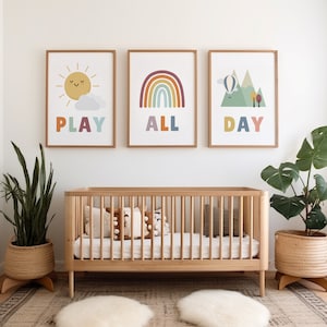 Puede incluir: Tres impresiones enmarcadas con ilustraciones y texto coloridos. Las impresiones dicen "Play All Day" y est&aacute;n colgadas sobre una cuna de madera con ropa de cama y almohadas blancas.