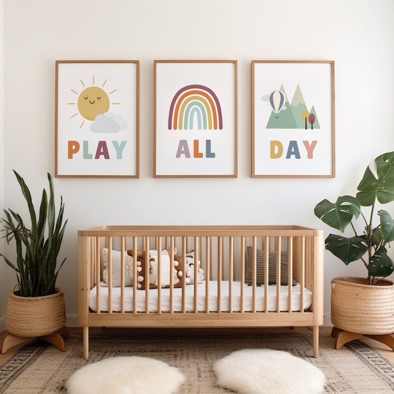 Puede incluir: Tres impresiones enmarcadas con ilustraciones y texto coloridos. Las impresiones dicen "Play All Day" y est&aacute;n colgadas sobre una cuna de madera con ropa de cama y almohadas blancas.