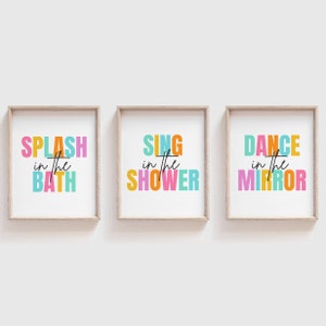 May include: Three framed prints with colorful text. The first print says "Splash in the Bath" in orange, pink, blue, and yellow. The second print says "Sing in the Shower" in orange, pink, blue, and yellow. The third print says "Dance in the Mirror" in orange, pink, blue, and yellow.