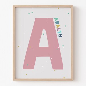 May include: A framed print featuring a large pink letter A and the name "ADALYN" written vertically in colourful letters. The background is white with small colourful dots.