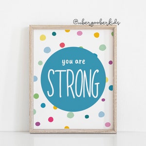 May include: A framed print with a blue circle on a white background with colourful polka dots. The circle says "you are STRONG" in white text.