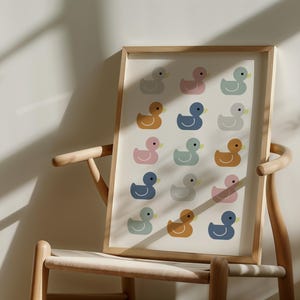 May include: A framed print featuring a pattern of colorful duck illustrations. The ducks are in shades of pink, blue, yellow, and gray, set against a cream background. The artwork is displayed on a wooden chair.