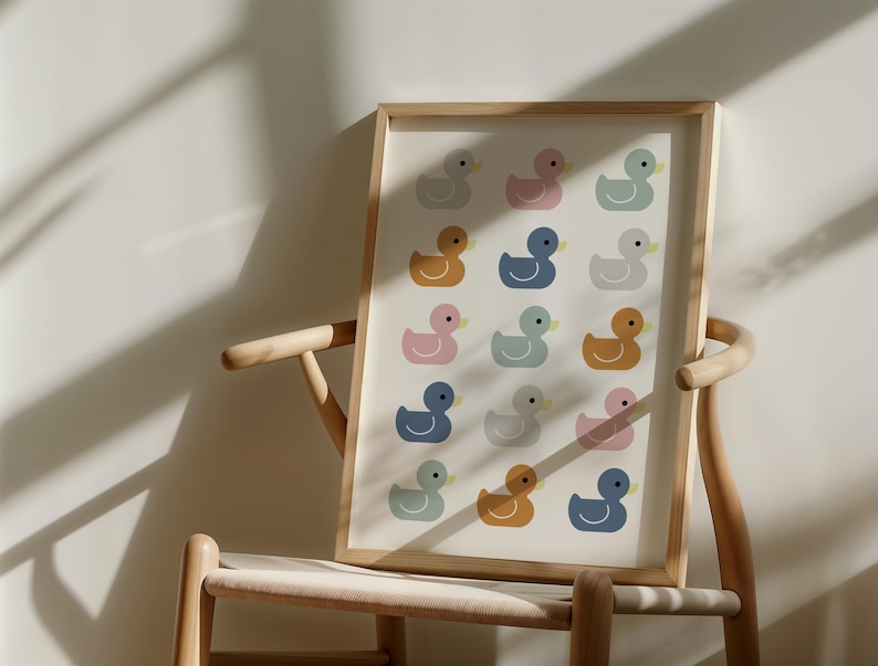 May include: A framed print featuring a pattern of colorful duck illustrations. The ducks are in shades of pink, blue, yellow, and gray, set against a cream background. The artwork is displayed on a wooden chair.