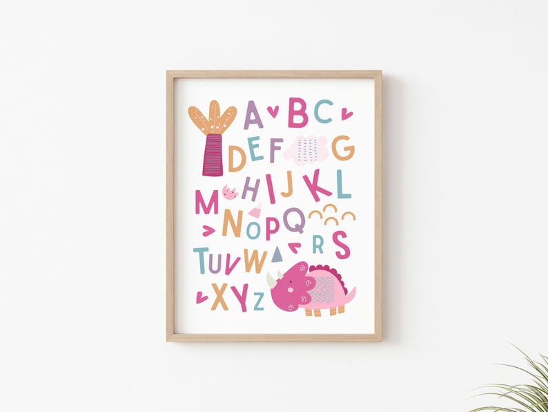 Puede incluir: Un p&oacute;ster de alfabeto colorido con un dinosaurio rosa y un cactus. Las letras est&aacute;n en diferentes colores y fuentes. El p&oacute;ster est&aacute; enmarcado en un marco de madera claro.