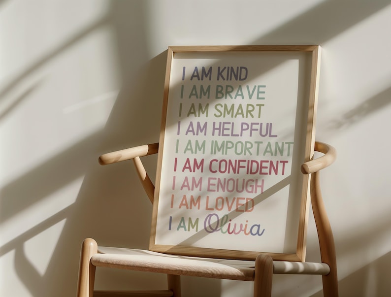 May include: A framed print with the text "I AM KIND, I AM BRAVE, I AM SMART, I AM HELPFUL, I AM IMPORTANT, I AM CONFIDENT, I AM ENOUGH, I AM LOVED, I AM Olivia" in rainbow colors on a white background.