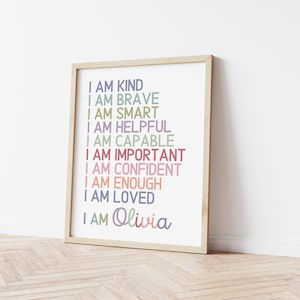 May include: A framed print with the text "I am kind, I am brave, I am smart, I am helpful, I am capable, I am important, I am confident, I am enough, I am loved, I am Olivia" in various pastel colors.