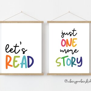May include: Two white framed prints with colorful text. The left print says "let's READ" in rainbow colors. The right print says "just ONE more STORY" in rainbow colors. The text on the right print is slightly blurry.