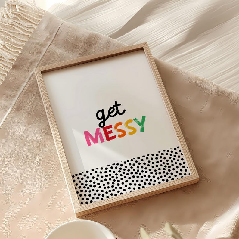 May include: A framed print with the text "get messy" in colorful letters on a white background. The bottom of the print has a black and white polka dot pattern.