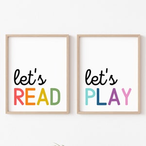 May include: Two framed prints with the text "let's" in black cursive font. The first print has the word "READ" in rainbow colours. The second print has the word "PLAY" in rainbow colours.