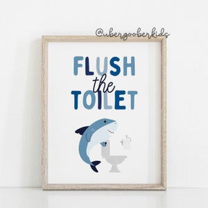 May include: A blue and white bathroom sign with a shark illustration and the text "FLUSH the TOILET".
