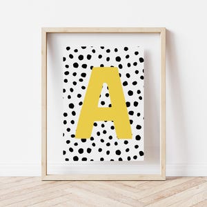 May include: A framed print with a white background and black polka dots. The letter "A" is in the centre of the print in a yellow colour.