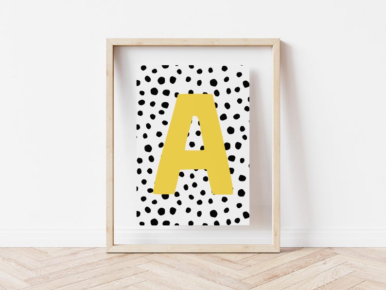 May include: A framed print with a white background and black polka dots. The letter "A" is in the centre of the print in a yellow colour.