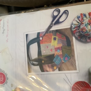 Op de afbeelding: Een naai-patroon voor een Crazy Patchwork Tote Bag van Margaret Lee. Het patroon bevat een foto van een kleurrijke patchwork-tas, een schaar, een naaldkussen en naai-accessoires.