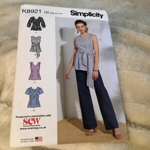 May include: Simplicity sewing pattern K8921 D5, sizes U.S. 4-12. The pattern features four top designs, including a sleeveless top with a tie, a top with a V-neck, and a wrap top. The pattern is designed and printed in the USA.