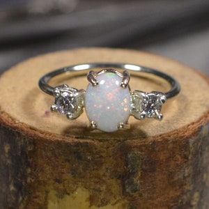 Könnte beinhalten: Ein silberner Ring mit einem weißen Opal-Edelstein und zwei kleineren weißen Edelsteinen auf jeder Seite.