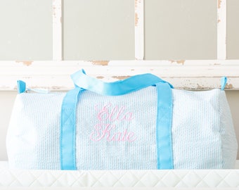 Puede incluir: Una bolsa de viaje de lona azul claro y blanco con asas azules y el nombre "Ella Kate" bordado en rosa.