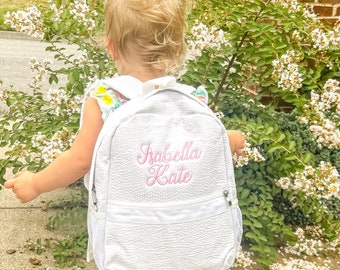 Könnte beinhalten: Weißer gesteppter Rucksack mit rosa gesticktem Text "Isabella Kate".