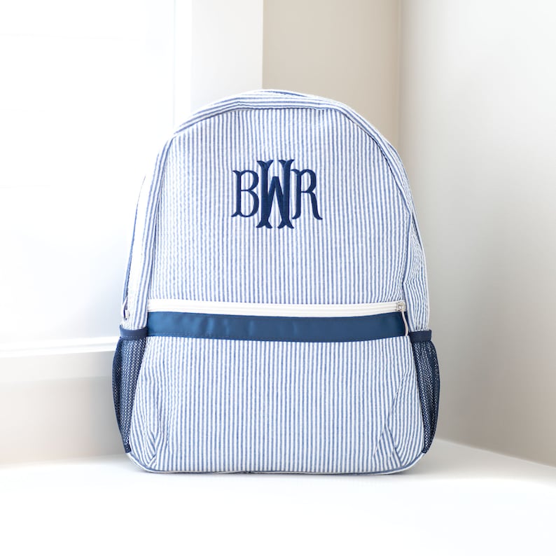 May include: A blue and white striped backpack with a navy blue zipper and a navy blue monogram that says "BWR" on the front.