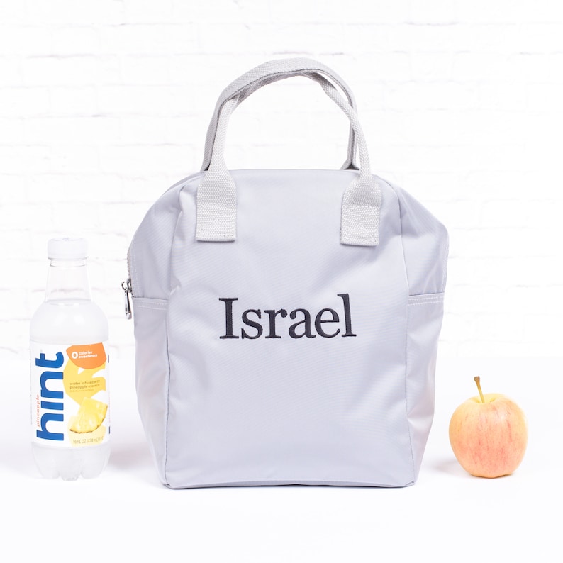 May include: A gray lunch bag with a white zipper and white handles. The bag has the name "Israel" embroidered on the front in black.