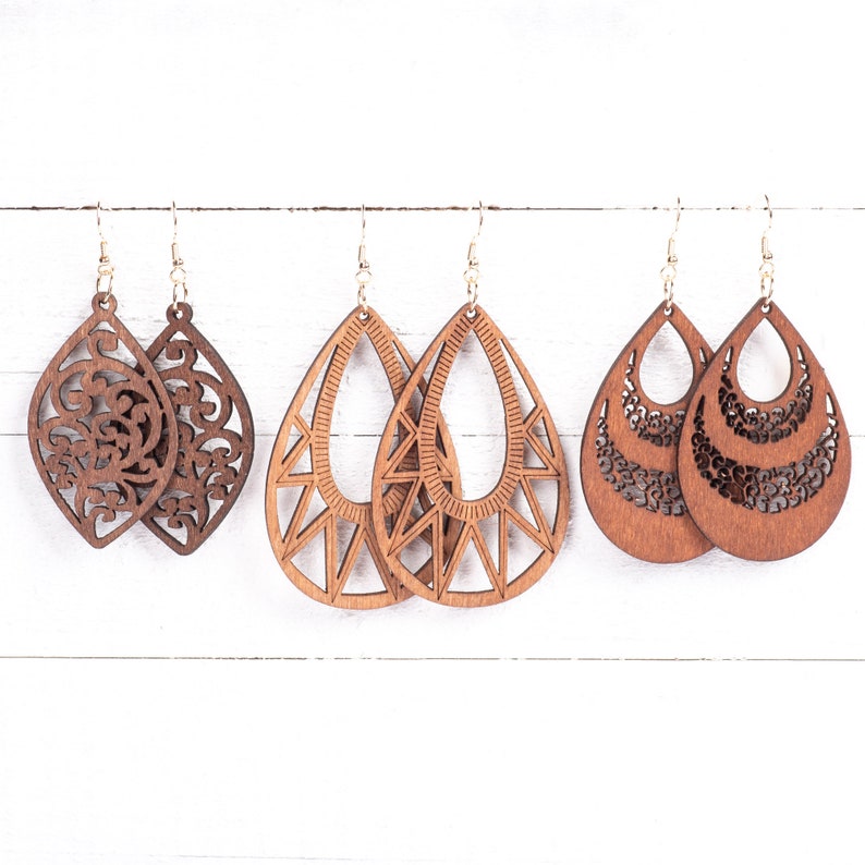 May include: Set of six wooden earrings in three different styles. Two earrings feature a floral design, two earrings feature a geometric design, and two earrings feature a layered design. All earrings are brown and have a natural wood finish.