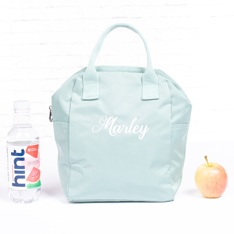 May include: A light blue insulated lunch bag with a white zipper and two white handles. The bag has the name "Marley" embroidered on the front in white cursive.