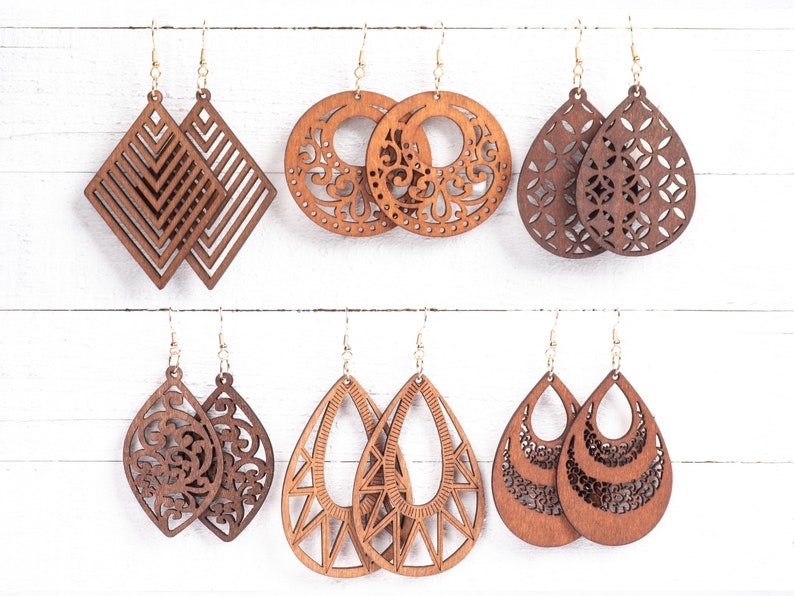 May include: Six pairs of wooden earrings with intricate laser-cut designs. The earrings are in various shapes, including teardrop, circle, and diamond. The wood is a rich brown color.
