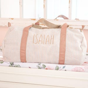 May include: A striped travel bag with pink handles and the name "ISAIAH" embroidered on the front.