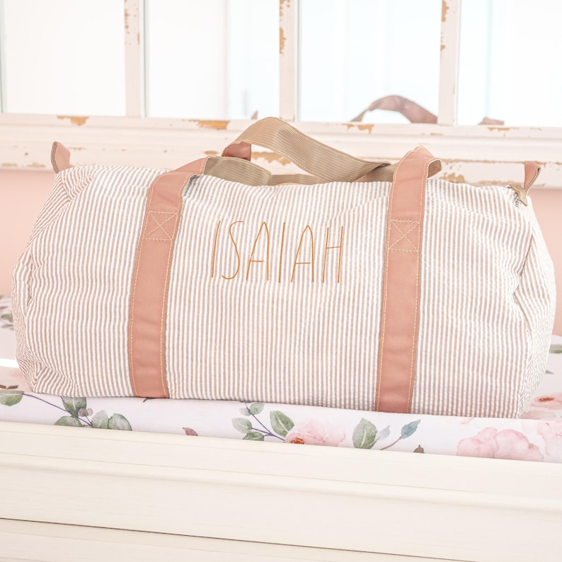 May include: A striped travel bag with pink handles and the name "ISAIAH" embroidered on the front.