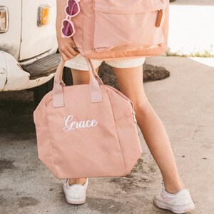 May include: A pink canvas tote bag with a white zipper and the name "Grace" embroidered on the front.