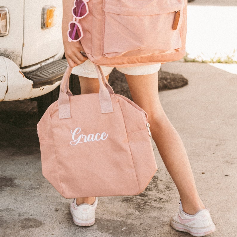 May include: A pink canvas tote bag with a white zipper and the name "Grace" embroidered on the front.
