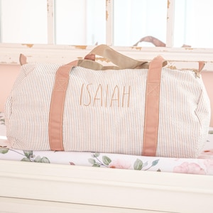 May include: A striped travel bag with pink handles and the name "ISAIAH" embroidered on the front.