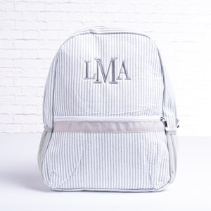 May include: A gray and white striped backpack with a gray zipper and a gray embroidered monogram that says "LMA".