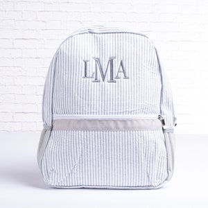 May include: A gray and white striped backpack with a gray zipper and a gray embroidered monogram "LMA" on the front.