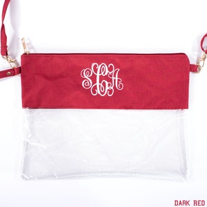 May include: A dark red clear crossbody bag with a gold zipper and a white monogram "SGA" on the front.