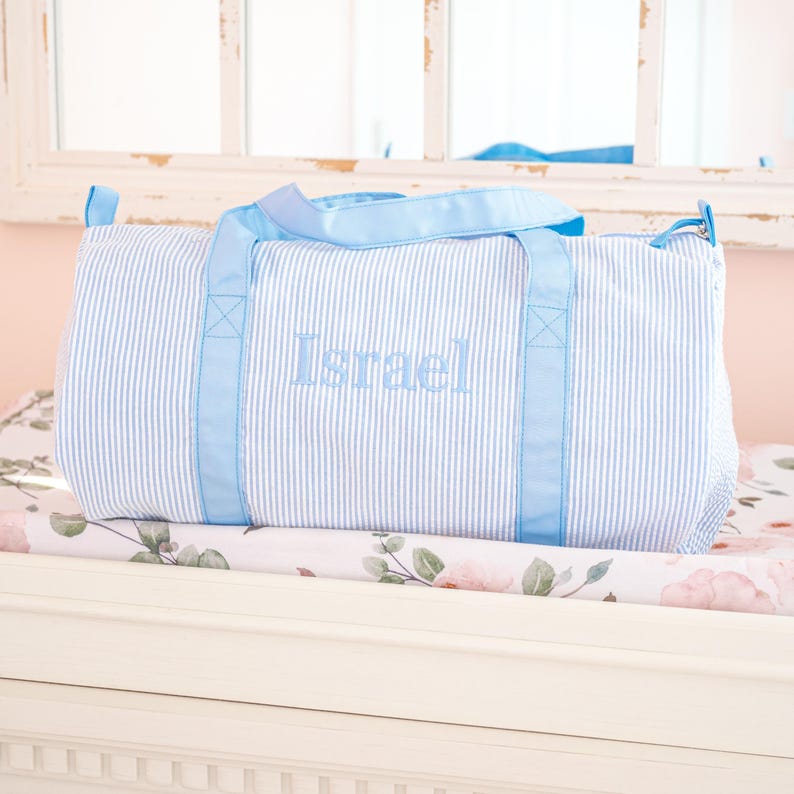 May include: A light blue striped duffel bag with blue handles and the name "Israel" embroidered on the front.