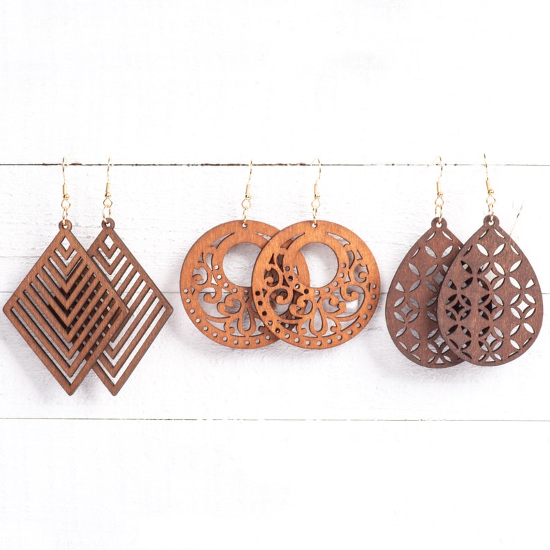 May include: Set of six wooden earrings in various shapes and designs. Two pairs feature a geometric diamond pattern, one pair has a circular design with intricate cutouts, and the final pair is teardrop shaped with a floral pattern.