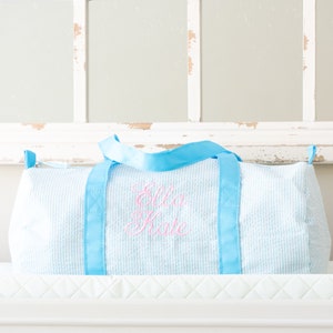 May include: A light blue and white gingham duffel bag with blue straps and the name "Ella Kate" embroidered in pink.
