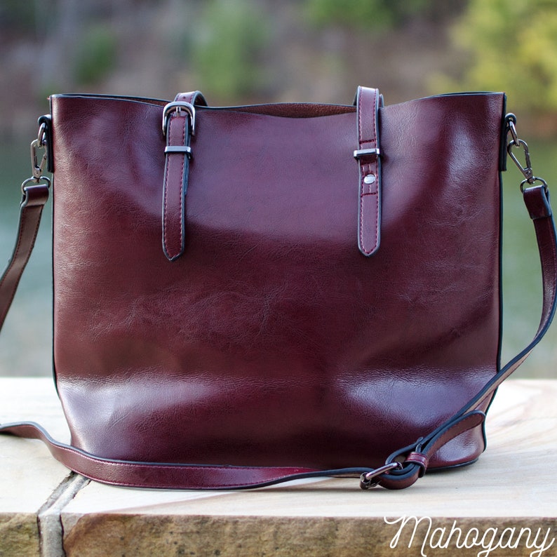 Pu&ograve; includere: Una borsa tote in pelle bordeaux con tracolla e due manici superiori. La borsa ha hardware color argento, tra cui fibbie e chiusure. La parola "Mahogany" &egrave; scritta in corsivo in basso.