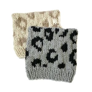 Puede incluir: Dos diademas de punto, una con un patrón geométrico beige y marrón y la otra con un estampado de leopardo gris y negro.