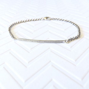 May include: A silver chain bracelet with a thin bar pendant set with small diamonds.
