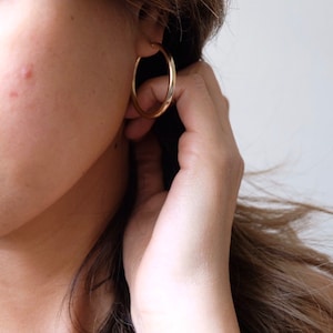 May include: A close-up of a person's ear with a gold hoop earring. The earring is simple and elegant, with a smooth, polished finish.