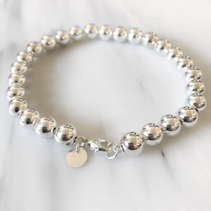 May include: A silver beaded bracelet with a silver clasp and a small silver tag.