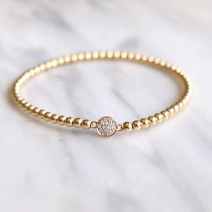 Puede incluir: Un brazalete de cuentas doradas con un pequeño dije redondo engastado con pequeñas piedras transparentes.