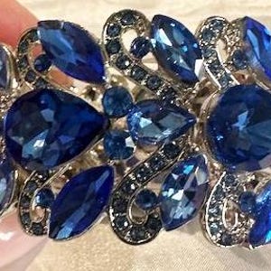 Peut inclure: Un bracelet en argent avec un motif floral et de gros cristaux bleus.