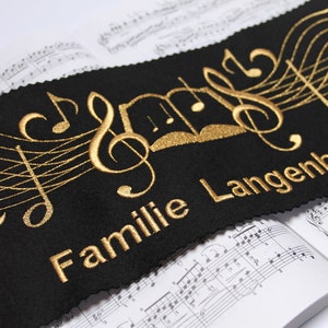 May include: Black fabric banner with gold embroidered musical notes and the text "Familie Langenbach".